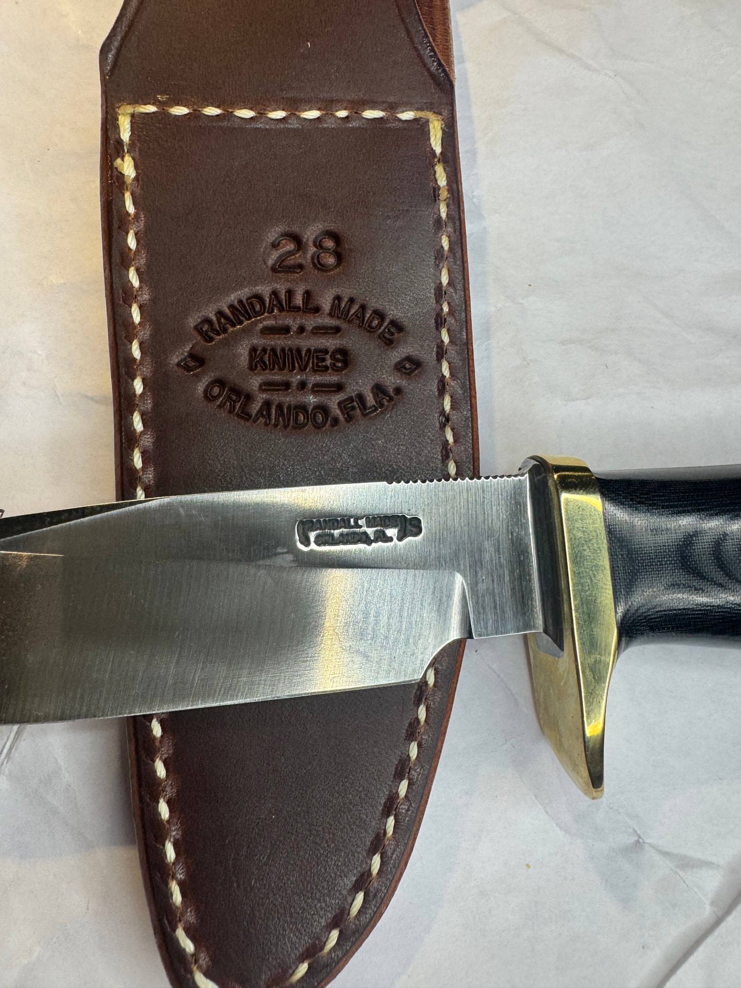 New in Paper Randall Model 28 Woodsman in Black Micarta. SS blade, brass single hilt. Lanyard. Brown leather sheath.