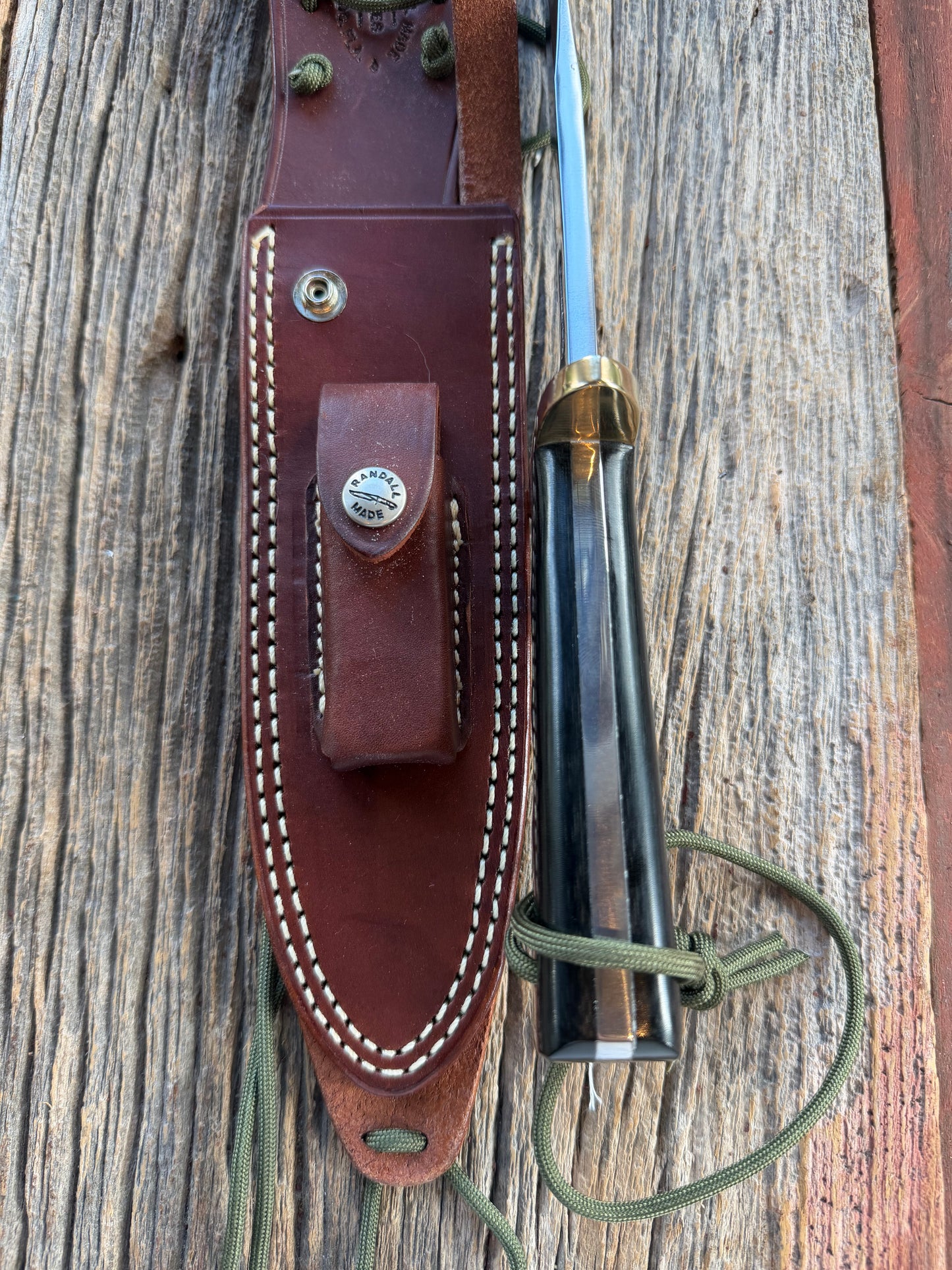 Randall Model 14-7.5 with a Black Micarta finger grooved handle. Carbon steel blade, Brass double hilt brown leather sheath.