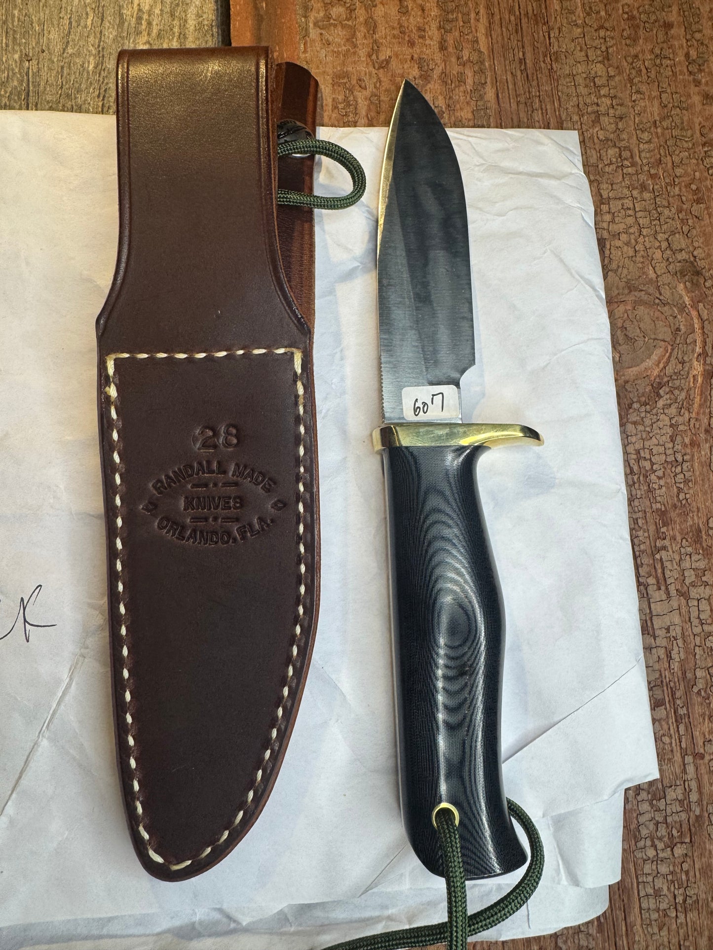 New in Paper Randall Model 28 Woodsman in Black Micarta. SS blade, brass single hilt. Lanyard. Brown leather sheath.