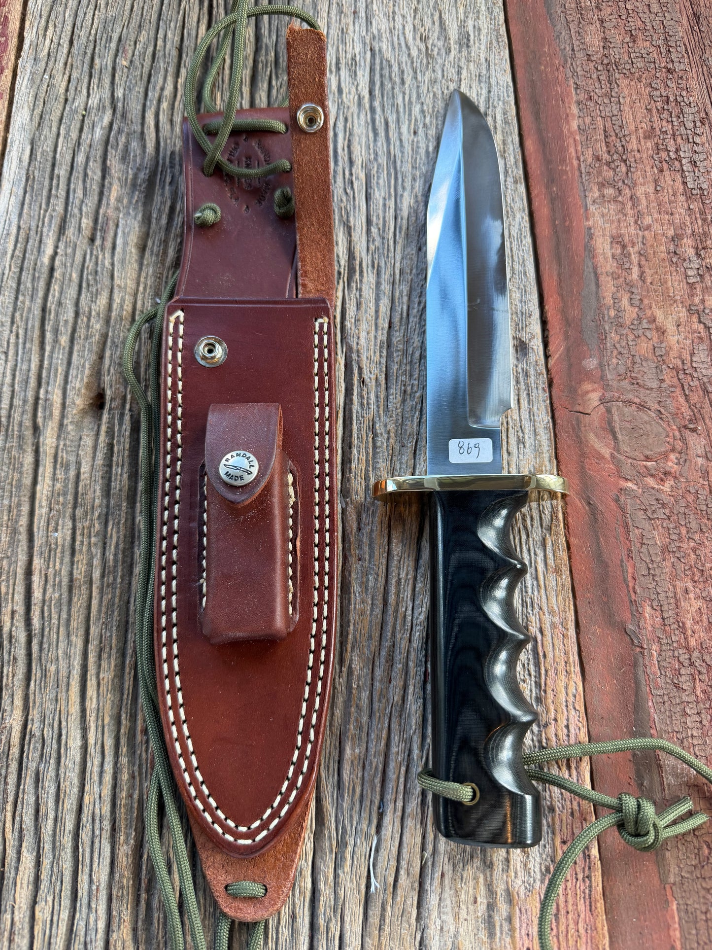Randall Model 14-7.5 with a Black Micarta finger grooved handle. Carbon steel blade, Brass double hilt brown leather sheath.