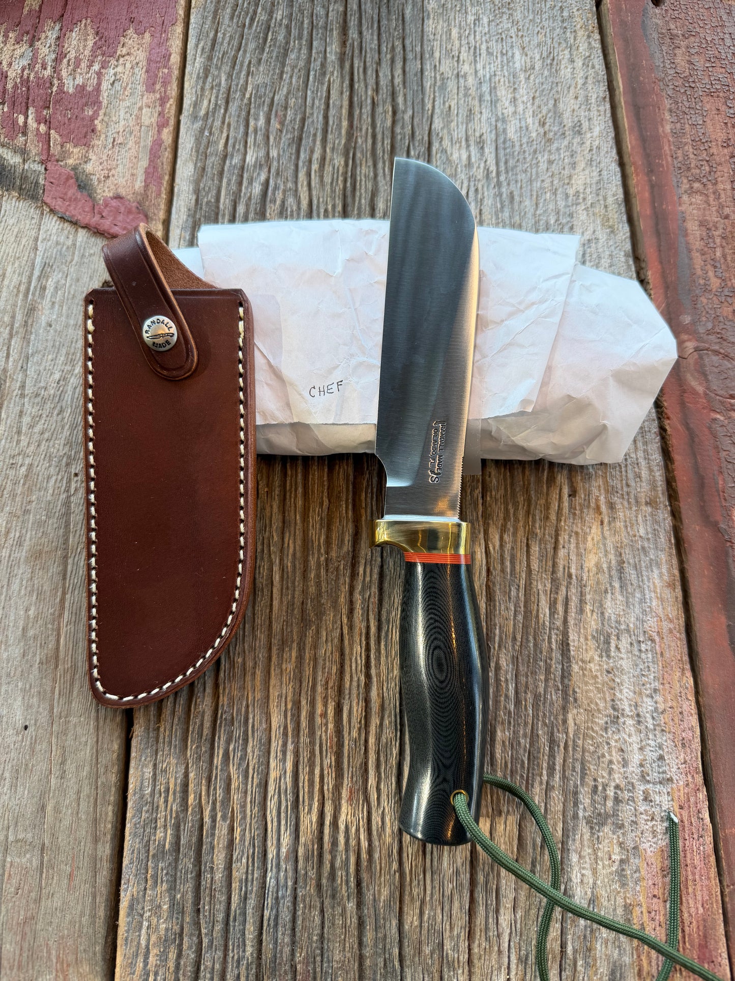 New in Paper Randall Chef’s Knife. Black Micarta in Brass with red spacers. Natural end, stainless steel blade and a lanyard.