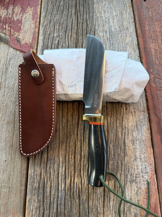 New in Paper Randall Chef’s Knife. Black Micarta in Brass with red spacers. Natural end, stainless steel blade and a lanyard.