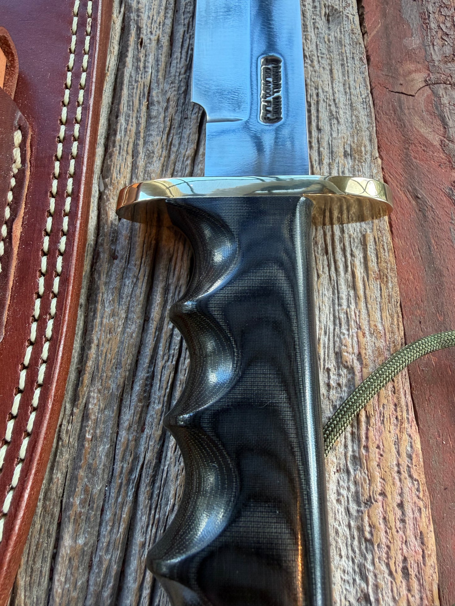 Randall Model 14-7.5 with a Black Micarta finger grooved handle. Carbon steel blade, Brass double hilt brown leather sheath.