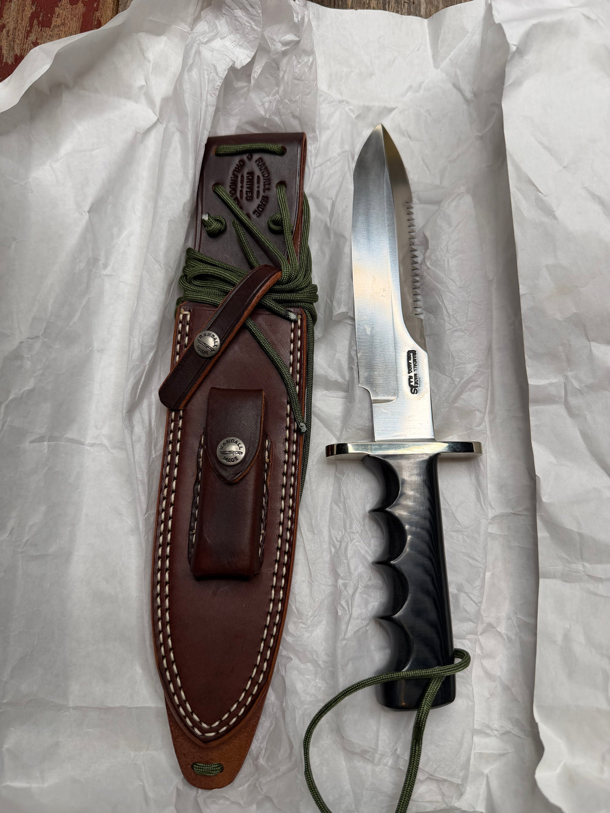 Randall Model 14-7.5 with a Black Micarta finger grooved handle. Stainless steel blade, Nickel double hilt brown leather sheath, Sawteeth, Lanyard.
