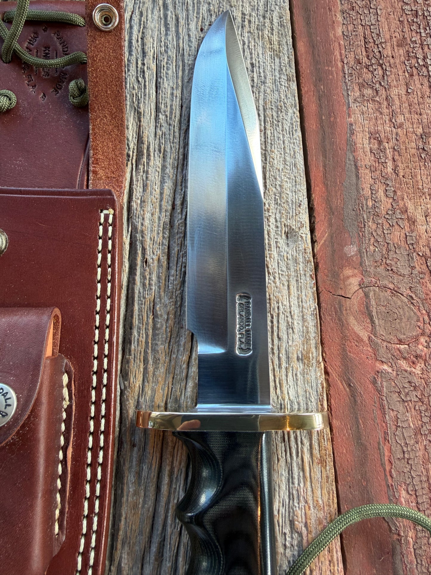 Randall Model 14-7.5 with a Black Micarta finger grooved handle. Carbon steel blade, Brass double hilt brown leather sheath.