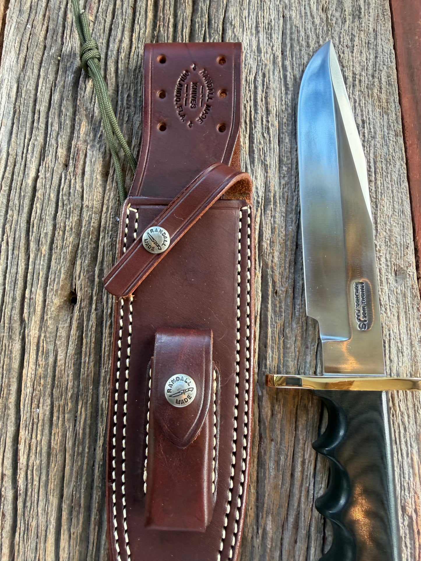 Randall Model 14-7.5 with a Black Micarta finger grooved handle. Stainless steel blade, Brass double hilt brown leather sheath.