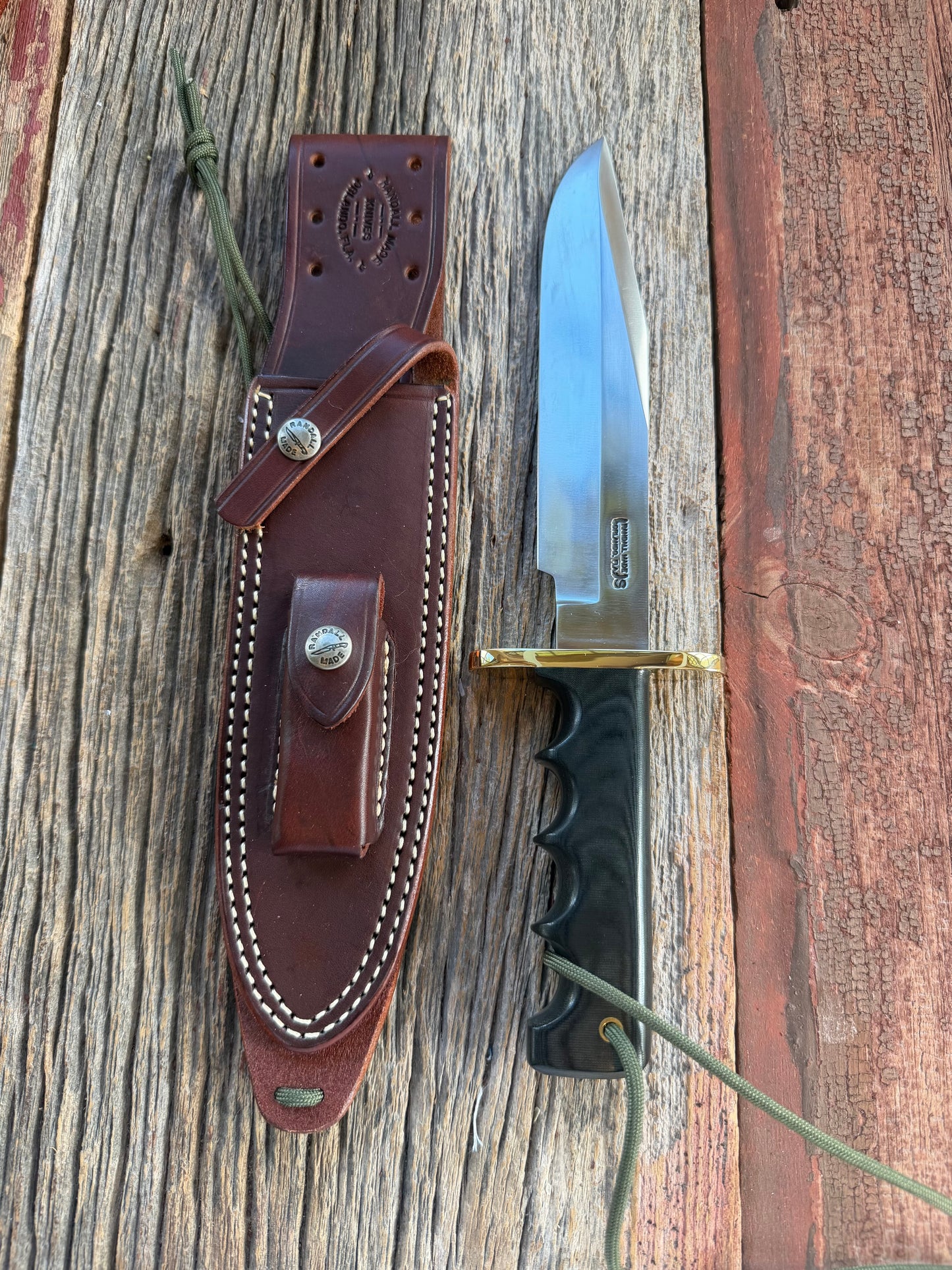 Randall Model 14-7.5 with a Black Micarta finger grooved handle. Stainless steel blade, Brass double hilt brown leather sheath.