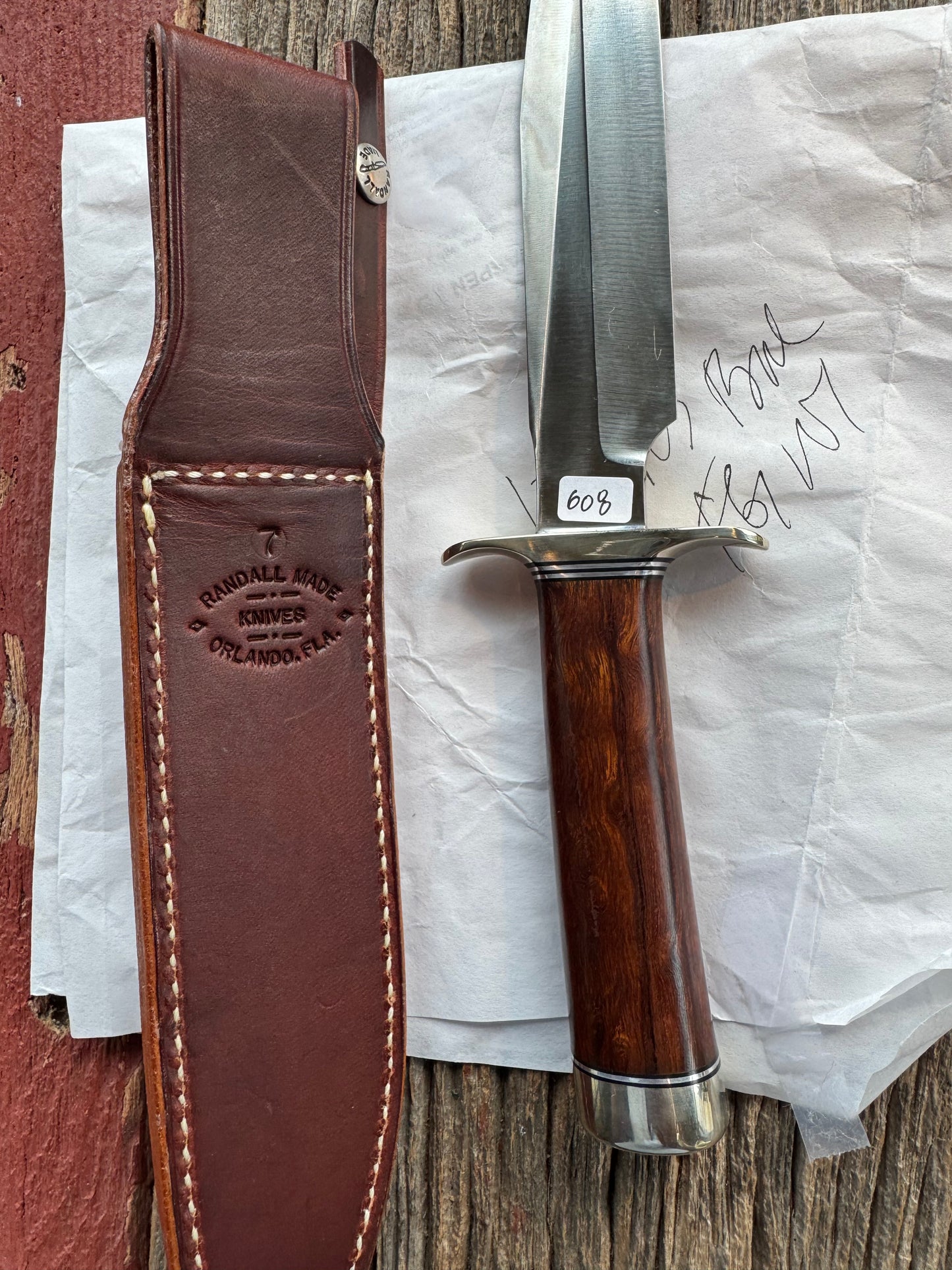 New in Paper Randall Model 1-7 Stainless steel blade, Nickel silver hilt and butt cap. Brown leather sheath. Burl wood handle.