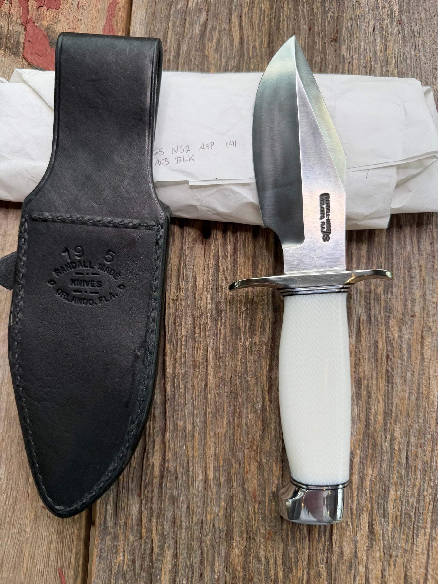 New in Paper Randall Model 19-5 Bushmaster with a White Ivorite handle. Stainless steel blade, Nickel silver hilt. Upgraded Black leather sheath. Crows Beak Aluminum handle.