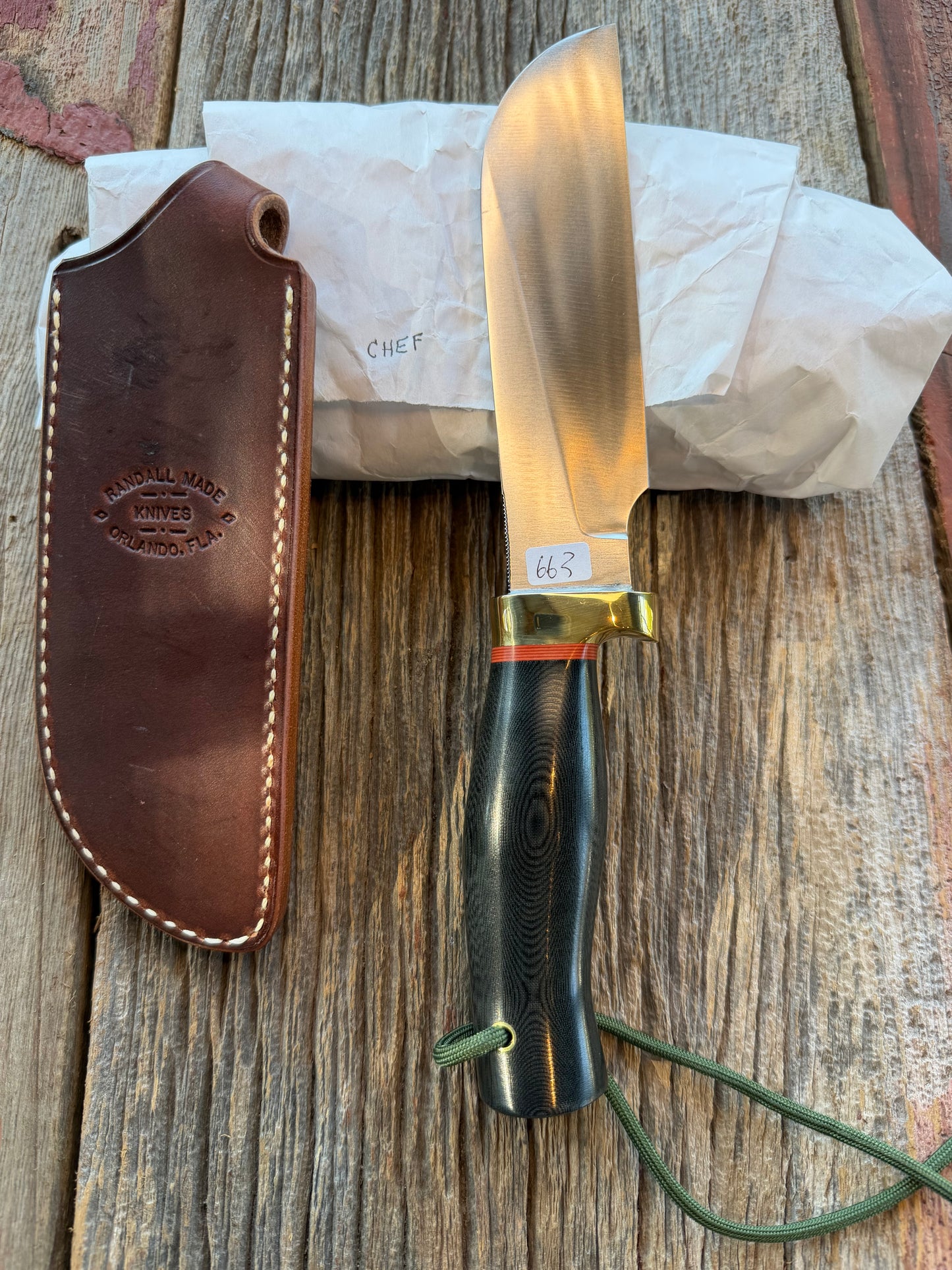 New in Paper Randall Chef’s Knife. Black Micarta in Brass with red spacers. Natural end, stainless steel blade and a lanyard.