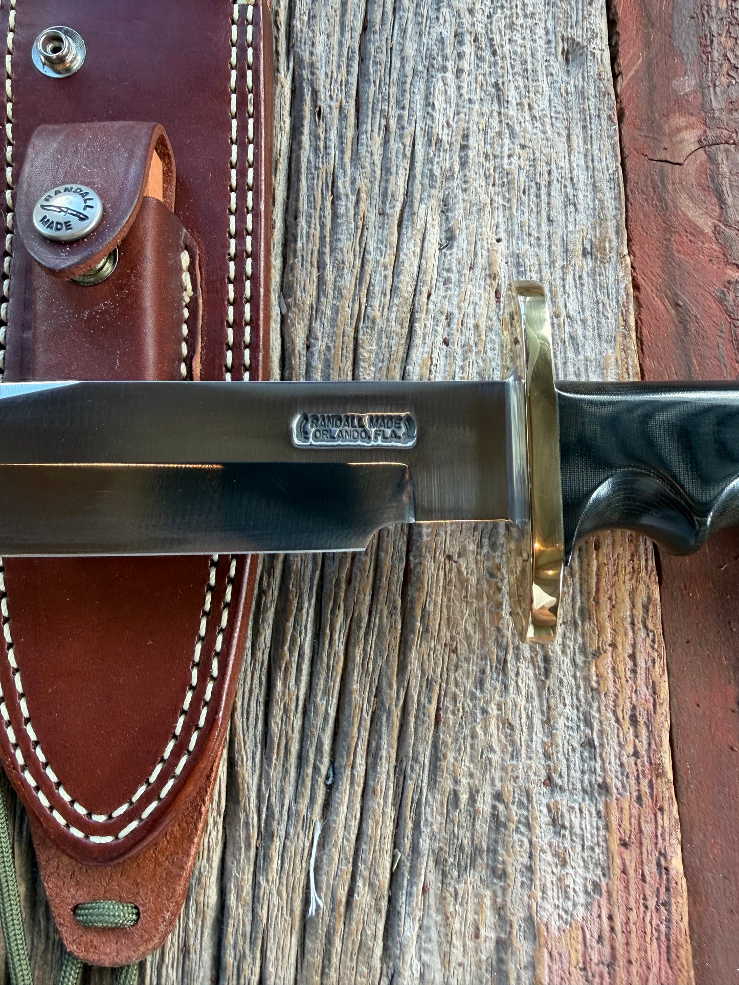 Randall Model 14-7.5 with a Black Micarta finger grooved handle. Carbon steel blade, Brass double hilt brown leather sheath.