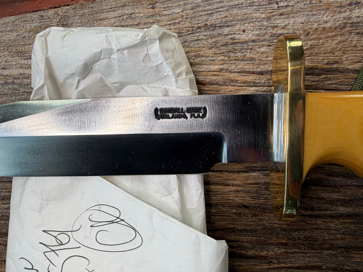 Randall Model 14-7.5 with a Yellow Micarta single finger handle. Carbon steel blade, brass double hilt, brown leather sheath, Lanyard.