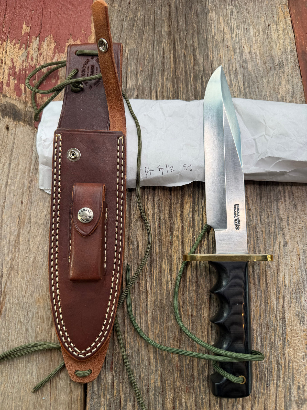 Randall Model 14-7.5 with a Black Micarta finger grooved handle. Stainless steel blade, brass double hilt brown leather sheath, Lanyard.