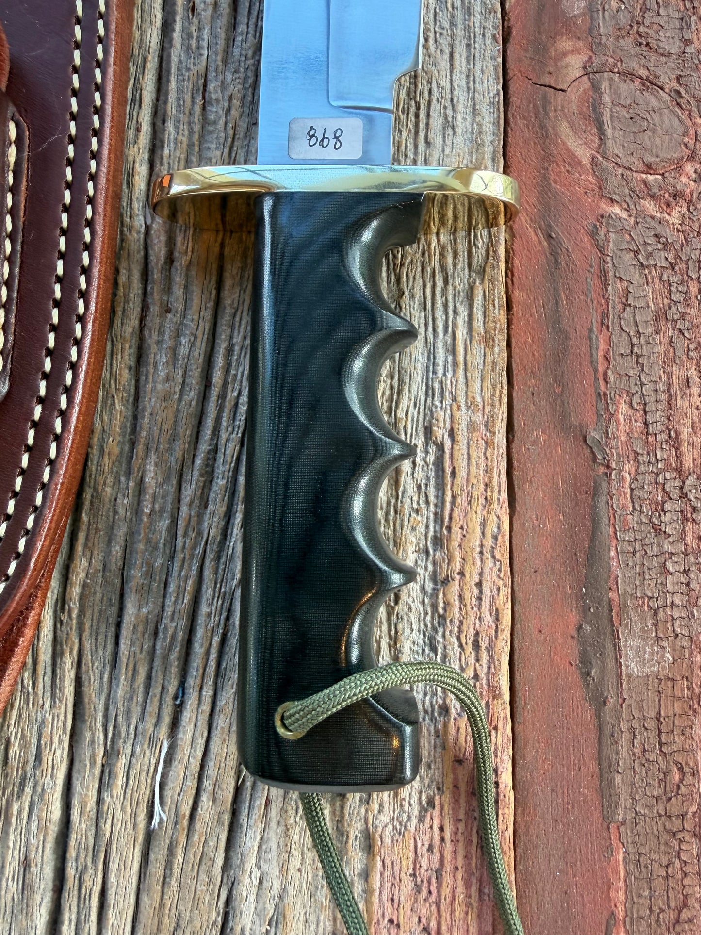 Randall Model 14-7.5 with a Black Micarta finger grooved handle. Stainless steel blade, Brass double hilt brown leather sheath.
