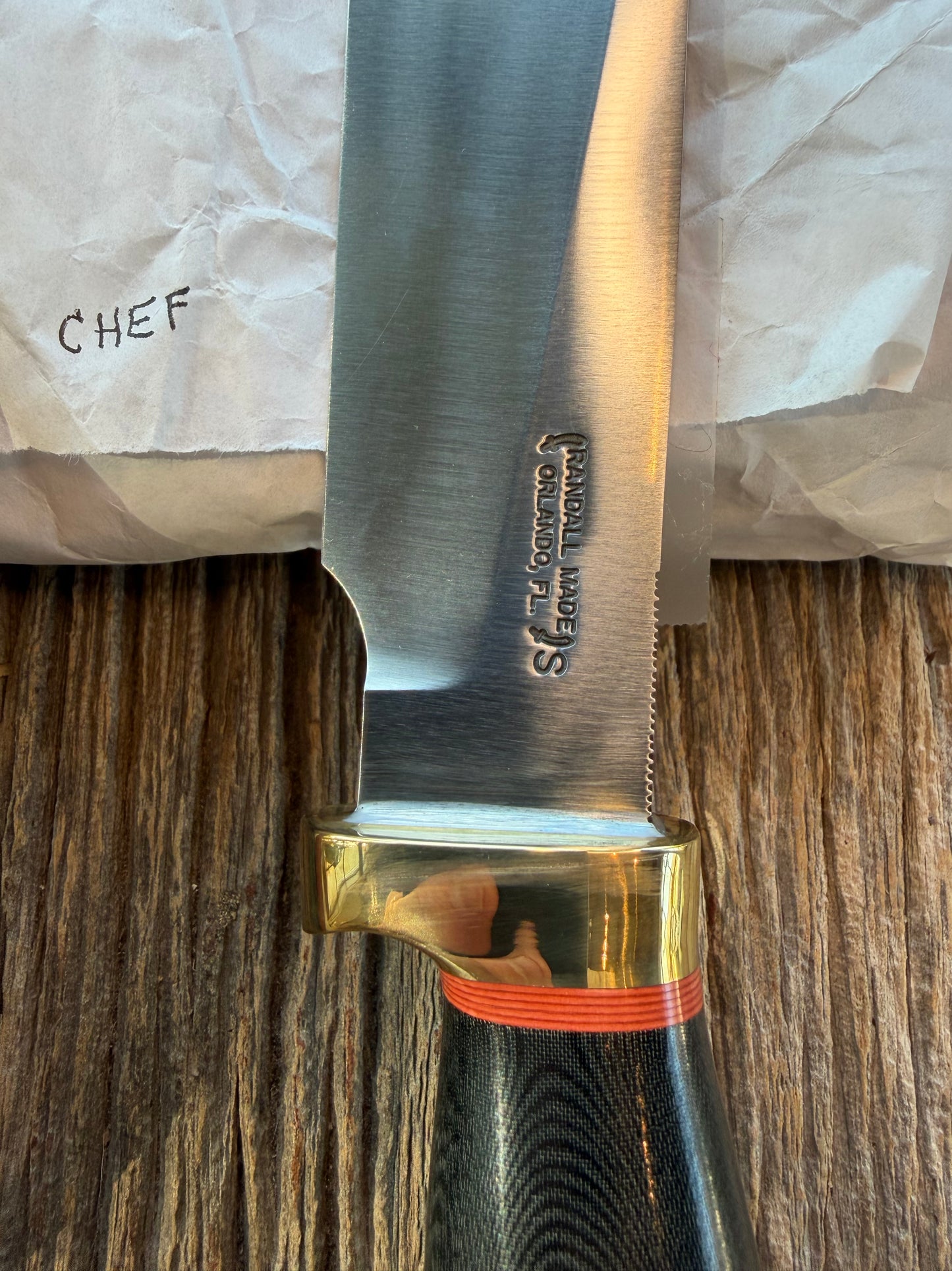 New in Paper Randall Chef’s Knife. Black Micarta in Brass with red spacers. Natural end, stainless steel blade and a lanyard.
