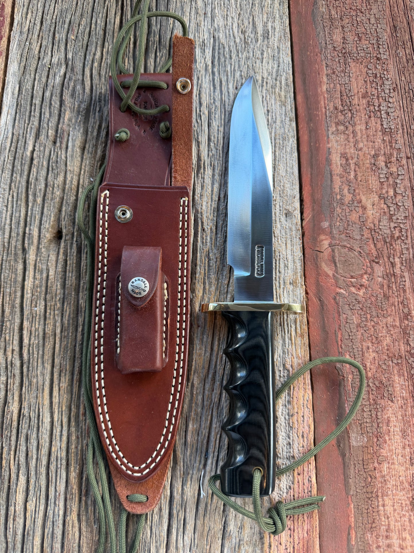Randall Model 14-7.5 with a Black Micarta finger grooved handle. Carbon steel blade, Brass double hilt brown leather sheath.