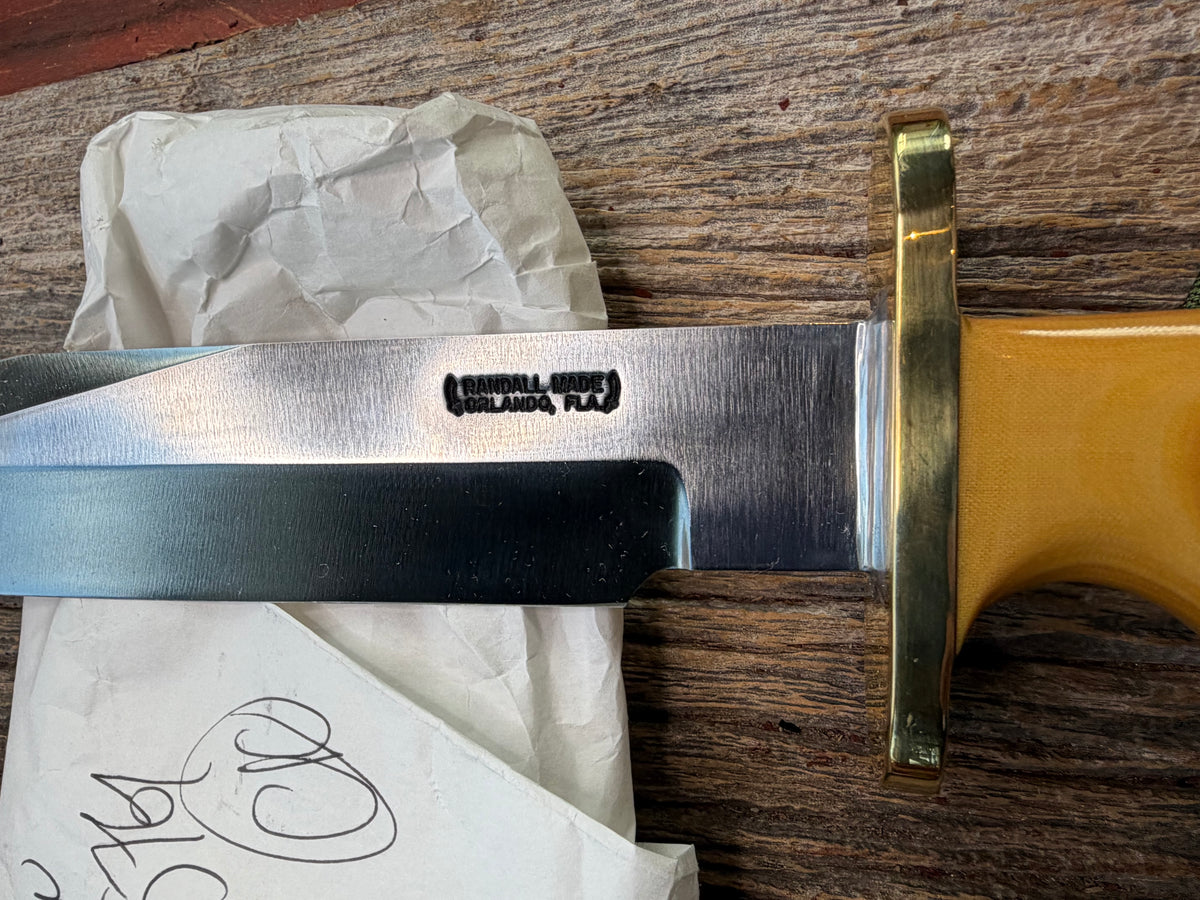 Randall Model 14-7.5 with a Yellow Micarta single finger handle. Carbon steel blade, brass double hilt, brown leather sheath, Lanyard.
